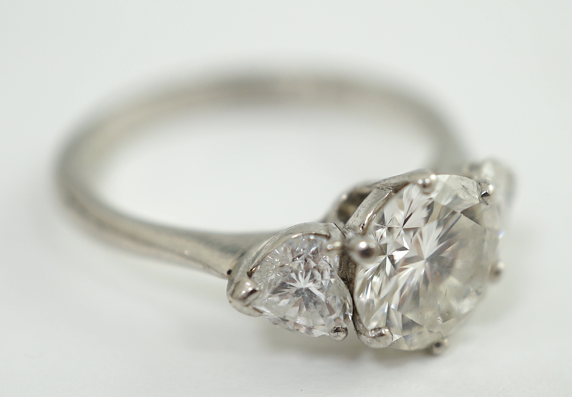 A modern platinum and single stone diamond ring, with two stone heart shaped diamond set shoulders